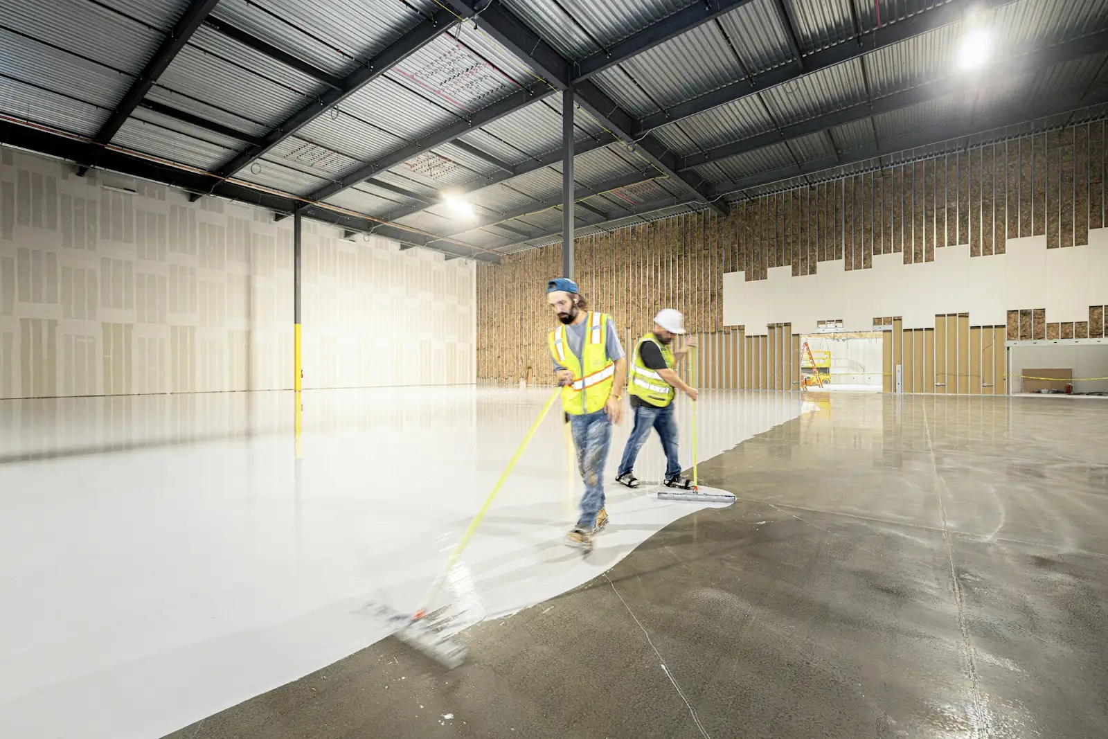 Two installers squeegeeing a fresh epoxy coat across a commercial floor